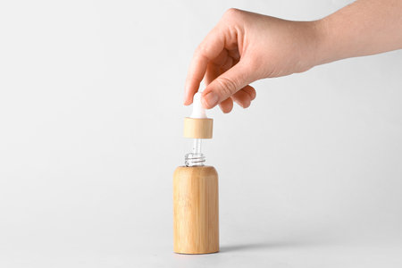 Female hand with bottle of serum on light background