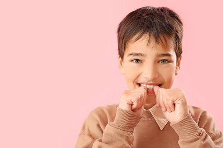 Little boy biting nails on pink background, closeup
