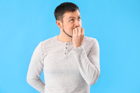 Handsome man biting nails on blue backgroundの写真素材