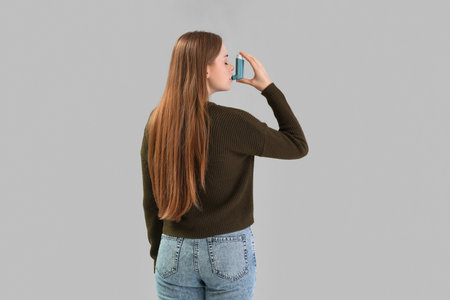 Young woman with inhaler on gray backgroundの写真素材