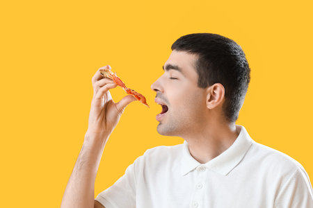 Young man eating tasty pizza on yellow background, closeupの写真素材
