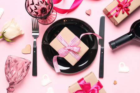 Plate with gift for Valentine's Day celebration, glasses and bottle of wine on pink backgroundの写真素材