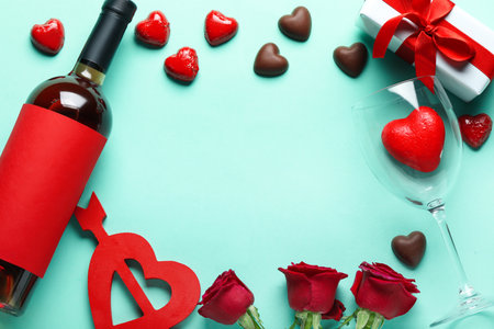 Frame made of wine bottle, chocolate candies and rose flowers on turquoise background. Valentine's Day celebrationの写真素材