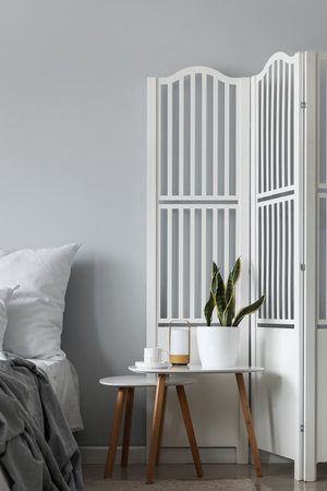 Bedside tables with houseplant and cup in light bedroom
