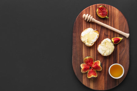 Wooden board of tasty sandwiches with cream cheese, honey and fresh fig on dark background