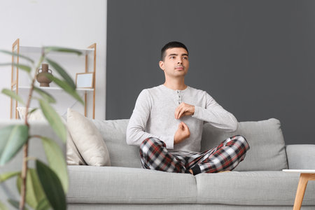 Young man in pajamas meditating on sofa at homeの写真素材