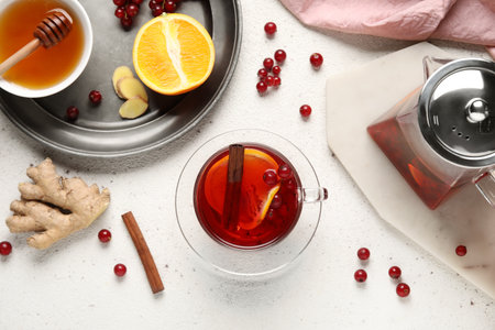 Tray with glass cup of fruit tea, red currant, honey, orange and teapot on light backgroundの写真素材
