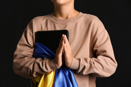 Little boy with Holy Bible and flag of Ukraine praying on black background, closeupの写真素材