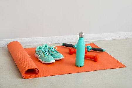 Sports water bottle with equipment and sneakers on mat near light wallの写真素材