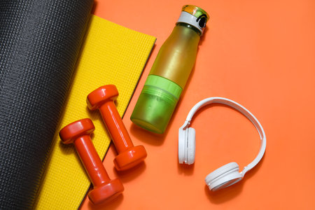 Sports water bottle with dumbbells, mat and headphones on red backgroundの写真素材