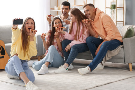 Group of friends with pizza taking selfie in living roomの写真素材