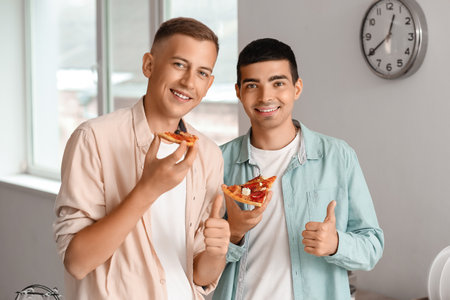 Male friends eating pizza in the kitchenの写真素材
