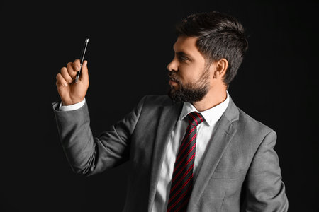 Young businessman in suit with pen on black backgroundの写真素材