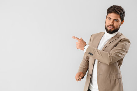 Handsome young businessman in beige jacket pointing at something on light backgroundの写真素材