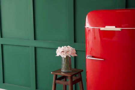 Stylish retro fridge and stool with flowers in vase near green wallの写真素材