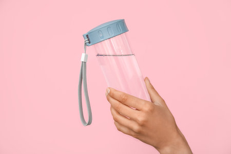 Female hand with bottle of water on pink background