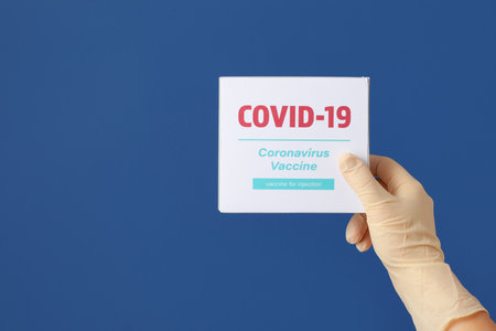 Doctor's hand with vaccine for immunization against COVID-19 on color backgroundの写真素材