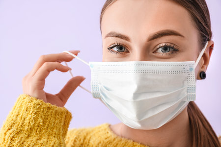 Young woman wearing medical mask on color backgroundの写真素材
