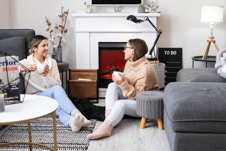Young women drinking tea near fireplace at homeの写真素材