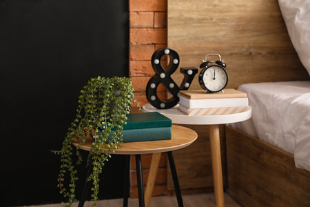 Tables with books, alarm clock and decor in the bedroom