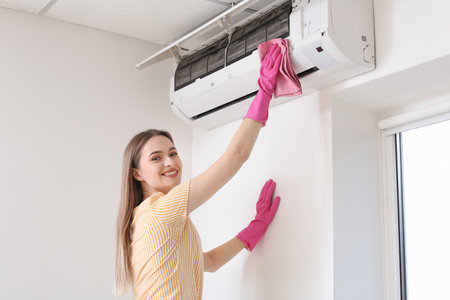 Beautiful young woman cleaning air conditioner at homeの写真素材