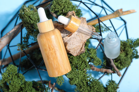 Stand with cosmetic dropper bottles, green moss and tree branches on blue backgroundの写真素材