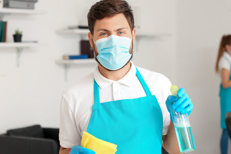 Male janitor with medical mask, rag and detergent in officeの写真素材