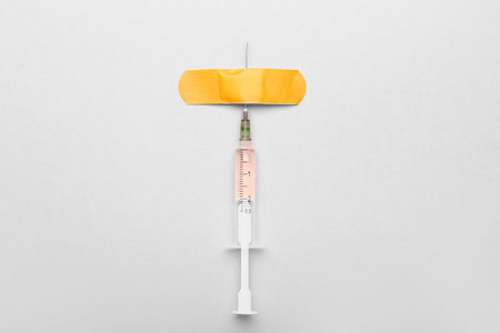 Medical syringe with remedy and plaster on light background