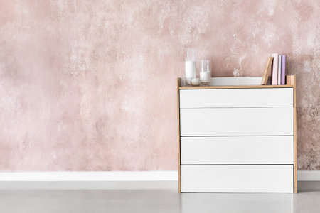 Stylish chest of drawers with candles and books near color wallの写真素材