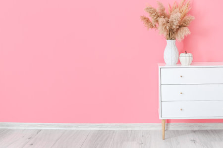 Chest of drawers with floral decor near color wall