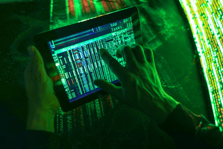 Hands of hacker with tablet computer on dark background