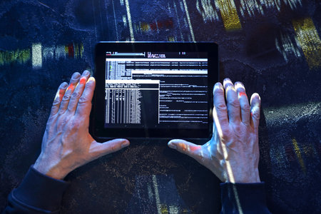 Hands of hacker with tablet computer on dark backgroundの写真素材