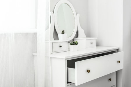 Chest of drawers with mirror near light wall in room