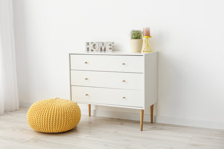 Modern chest of drawers and pouf near light wall in room