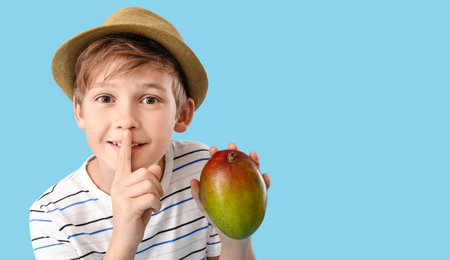 Cute little boy with fresh tasty mango on color backgroundの写真素材