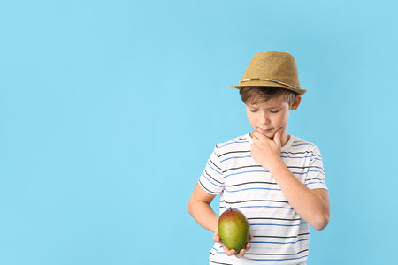 Cute little boy with fresh tasty mango on color backgroundの写真素材