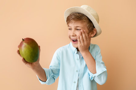 Cute little boy with fresh tasty mango on color backgroundの写真素材