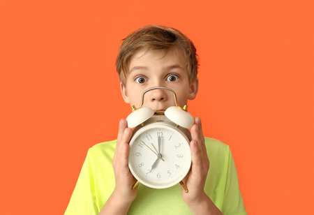 Little boy with alarm clock on color background