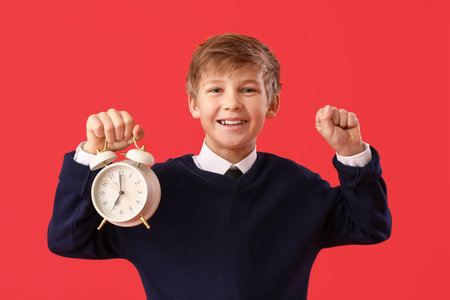 Happy little schoolboy with alarm clock on color backgroundの写真素材