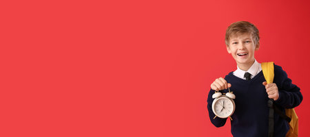 Happy little schoolboy with alarm clock on color backgroundの写真素材
