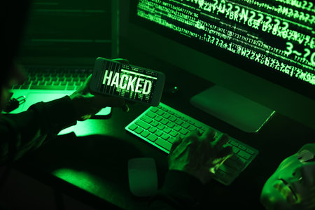 Hacker with mobile phone using computer in dark room