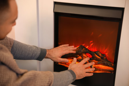 Handsome man warming hands near fireplace at homeの写真素材
