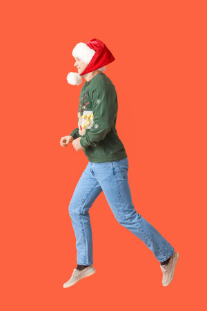 Jumping young man in Santa hat on color backgroundの写真素材