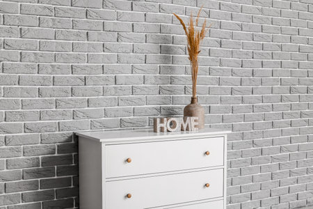Modern chest of drawers with vase and decor on brick background