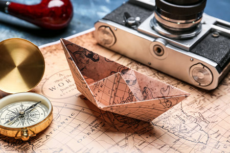 Paper boat, compass, photo camera and world map on color background, closeup