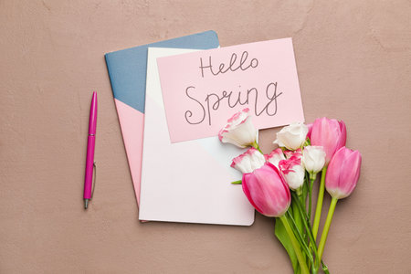 Notebooks, flowers and card with text HELLO SPRING on color background
