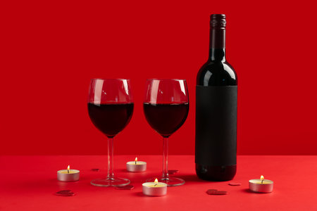 Glasses of wine, bottle and burning candles on red background. Valentine's Day Celebration