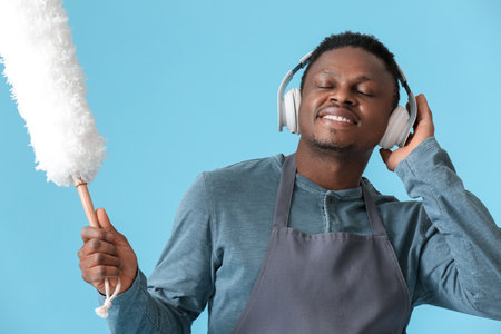 African-American man with dust brush listening to music on color background