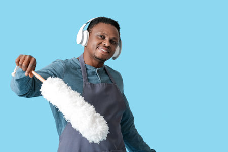 African-American man with dust brush listening to music on color background