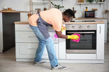 African-American man cleaning oven in kitchen